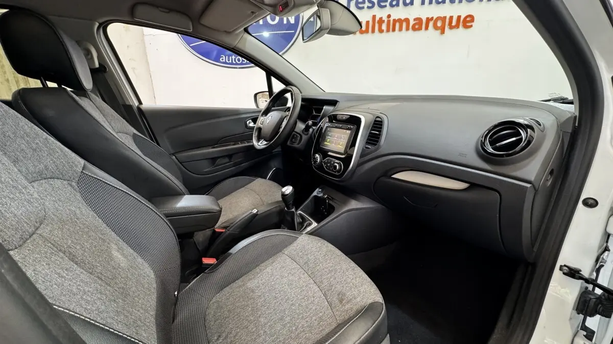 Vue intérieure côté conducteur du Renault Captur blanc 2019, montrant tableau de bord et sièges gris bi-matière.