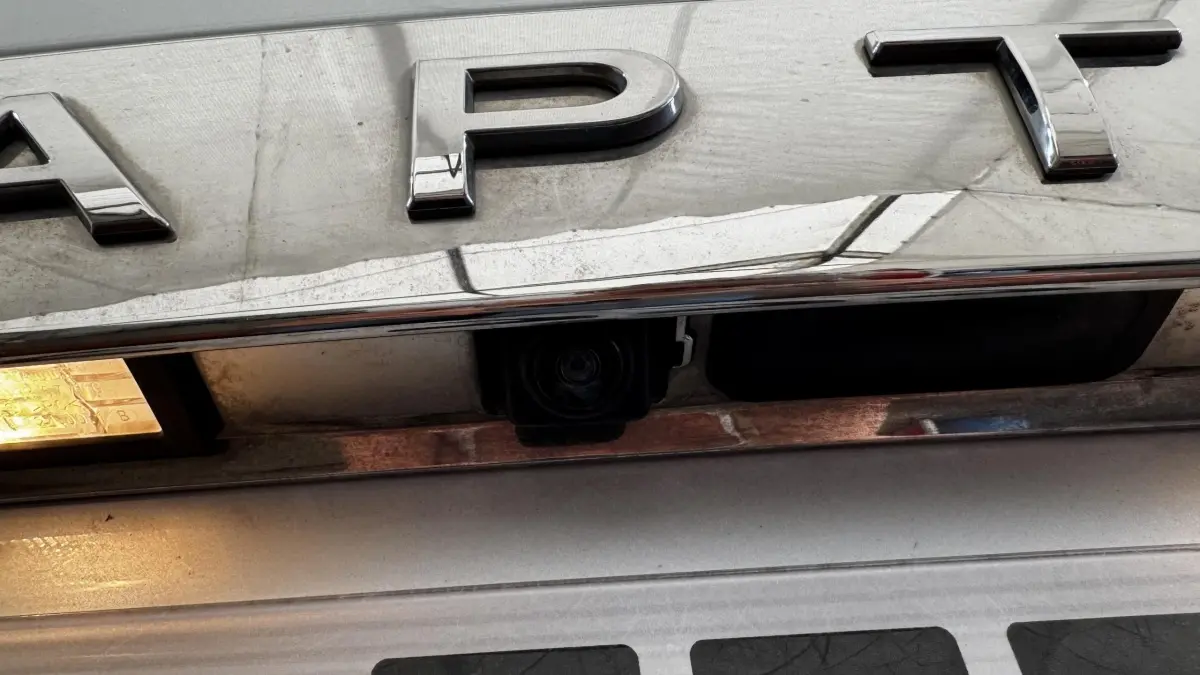 Gros plan sur la caméra de recul intégrée sous le logo chromé "CAPTUR" d'un Renault Captur blanc.