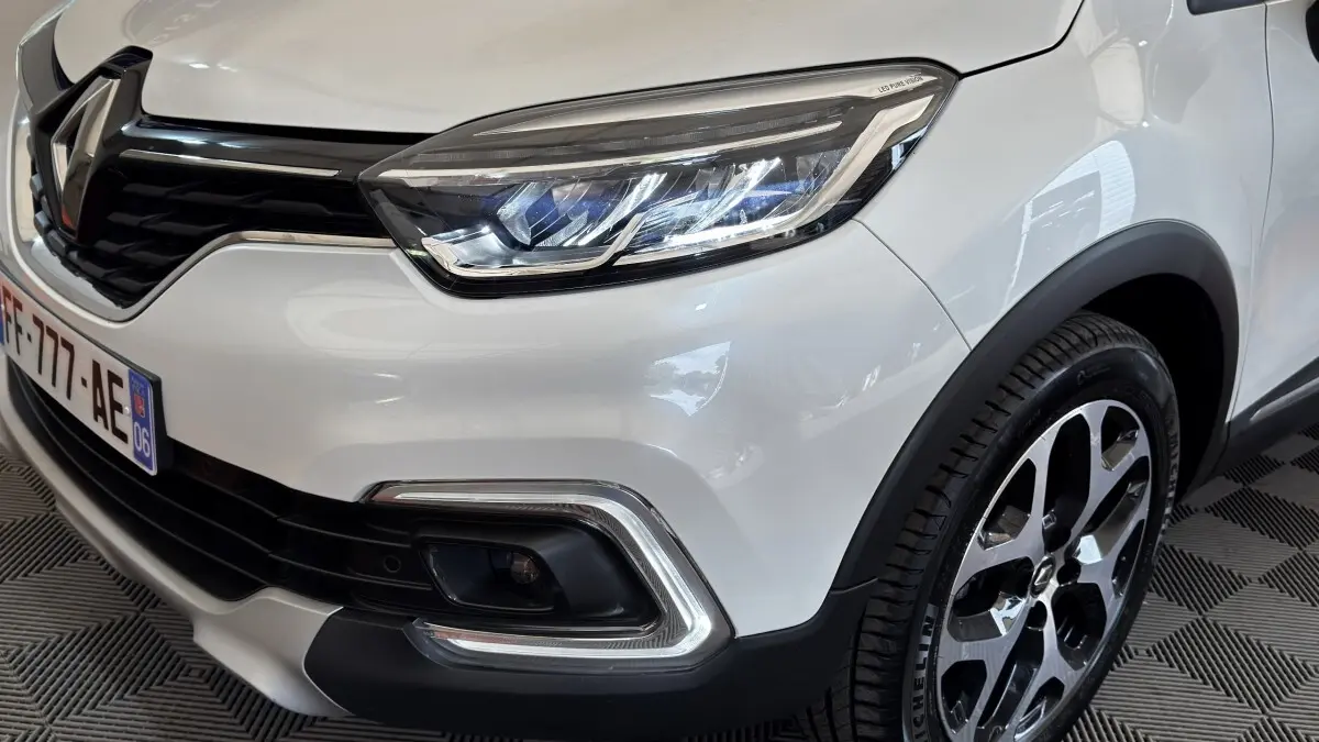 Gros plan sur l'avant droit blanc d'un Renault Captur Intens 2019, mettant en valeur le phare LED et la jante alliage.