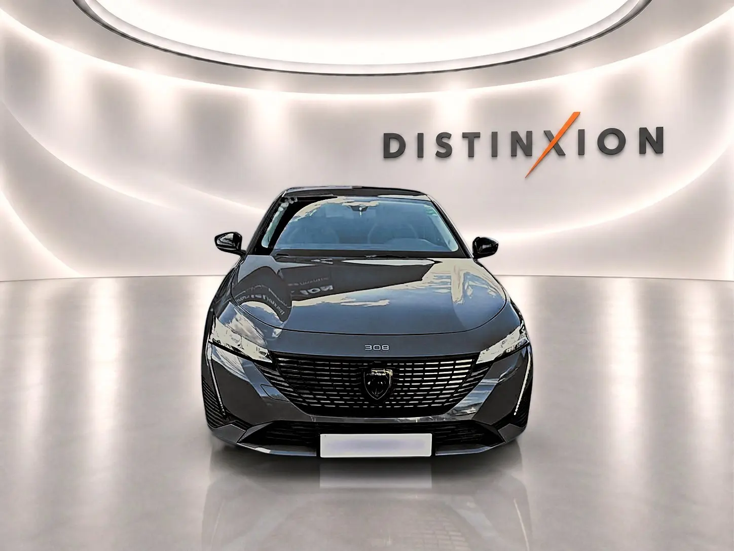 Vue frontale d'une Peugeot 308 gris selenium 2025 avec calandre noire et logo distinctif dans un showroom lumineux.