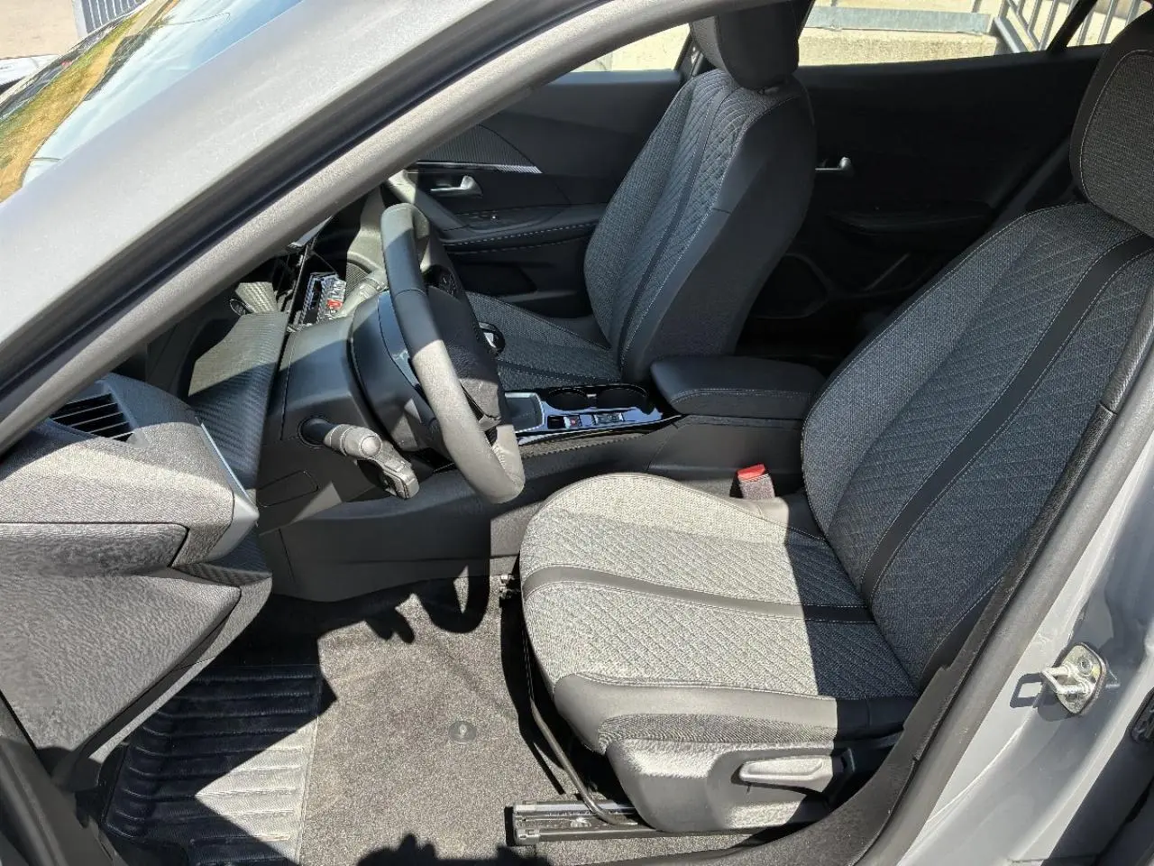 Vue intérieure côté conducteur du Peugeot 2008 2024 sellenium, montrant les sièges tissu gris et la console centrale.