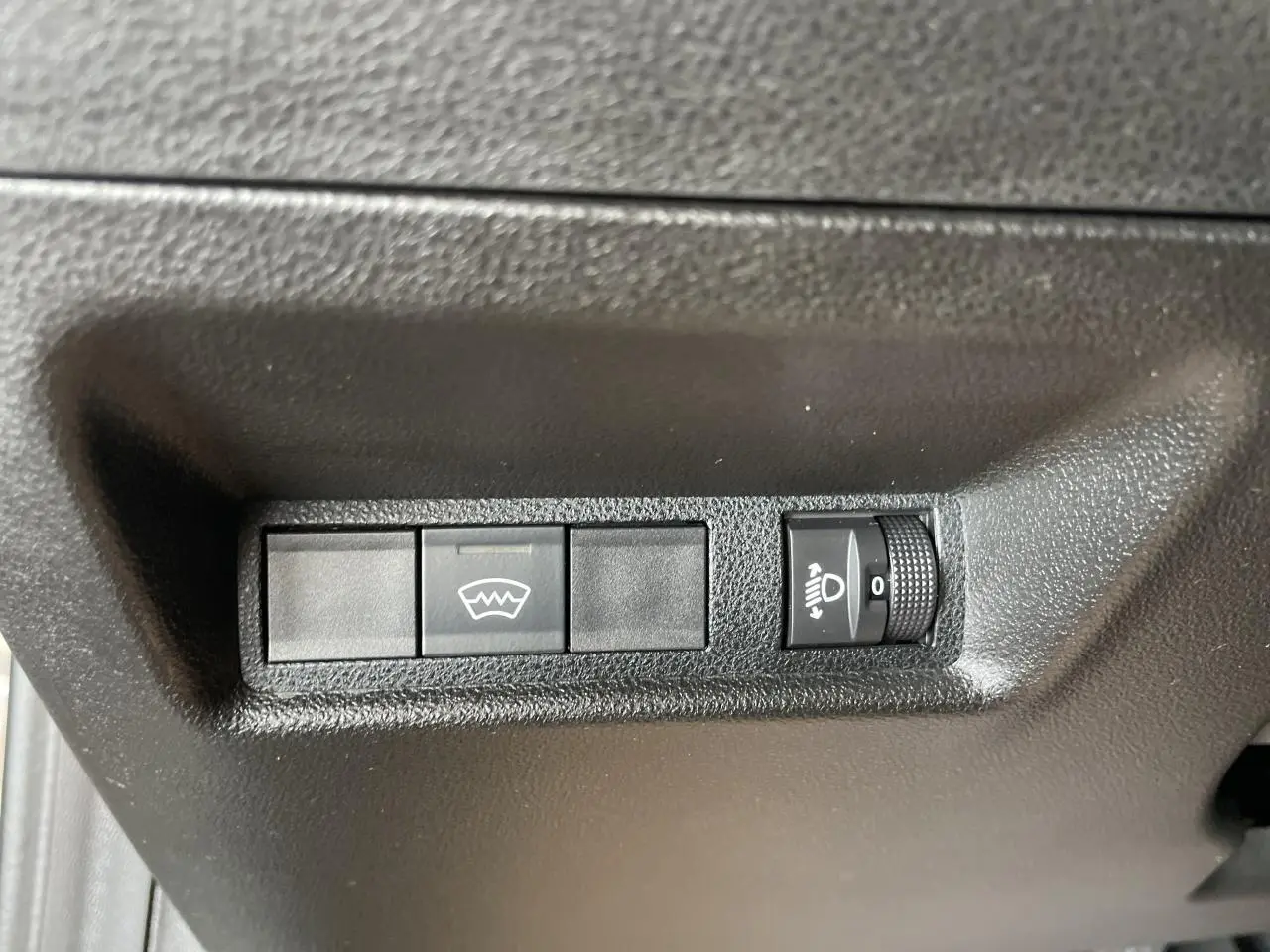 Gros plan sur les commandes de réglage des phares et dégivrage, intérieur noir de la Fiat 600 beige métallisé.