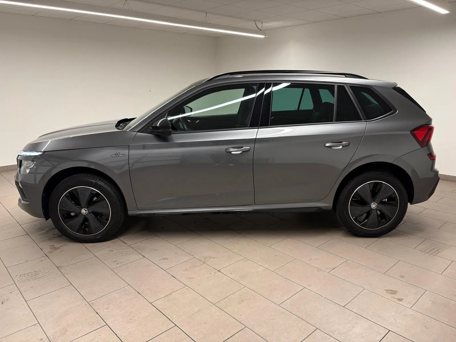 Vue de profil côté gauche d’un Skoda Kamiq 1.5 TSI Monte Carlo gris graphite avec jantes noires distinctives.