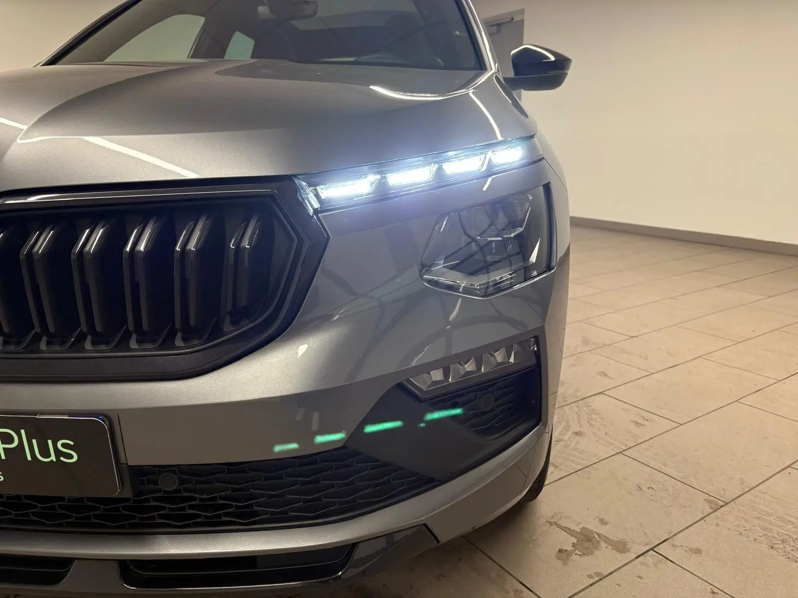 Gros plan sur l’avant droit du Skoda Kamiq Monte Carlo gris graphite 2024, mettant en valeur la calandre noire et les phares LED allumés.