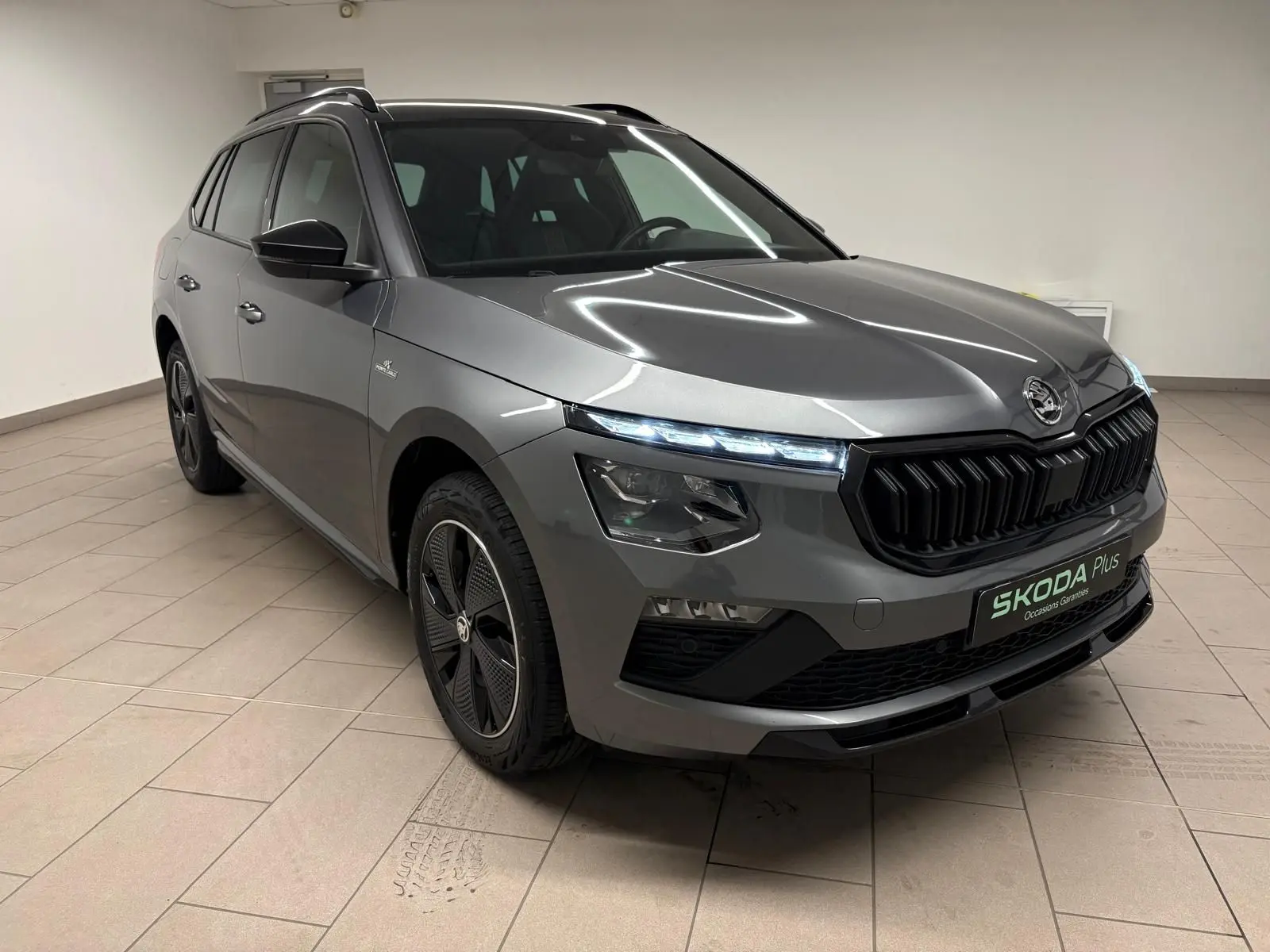 Vue 3/4 avant droite d’un Skoda Kamiq Monte Carlo 2024 gris graphite avec calandre noire et jantes spécifiques.