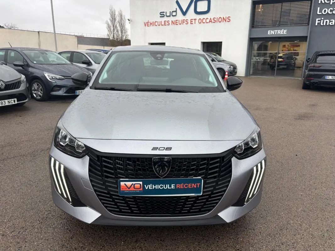 Vue avant d'une Peugeot 208 gris clair 2025 avec feux diurnes LED en forme de griffes et calandre noire distinctive.