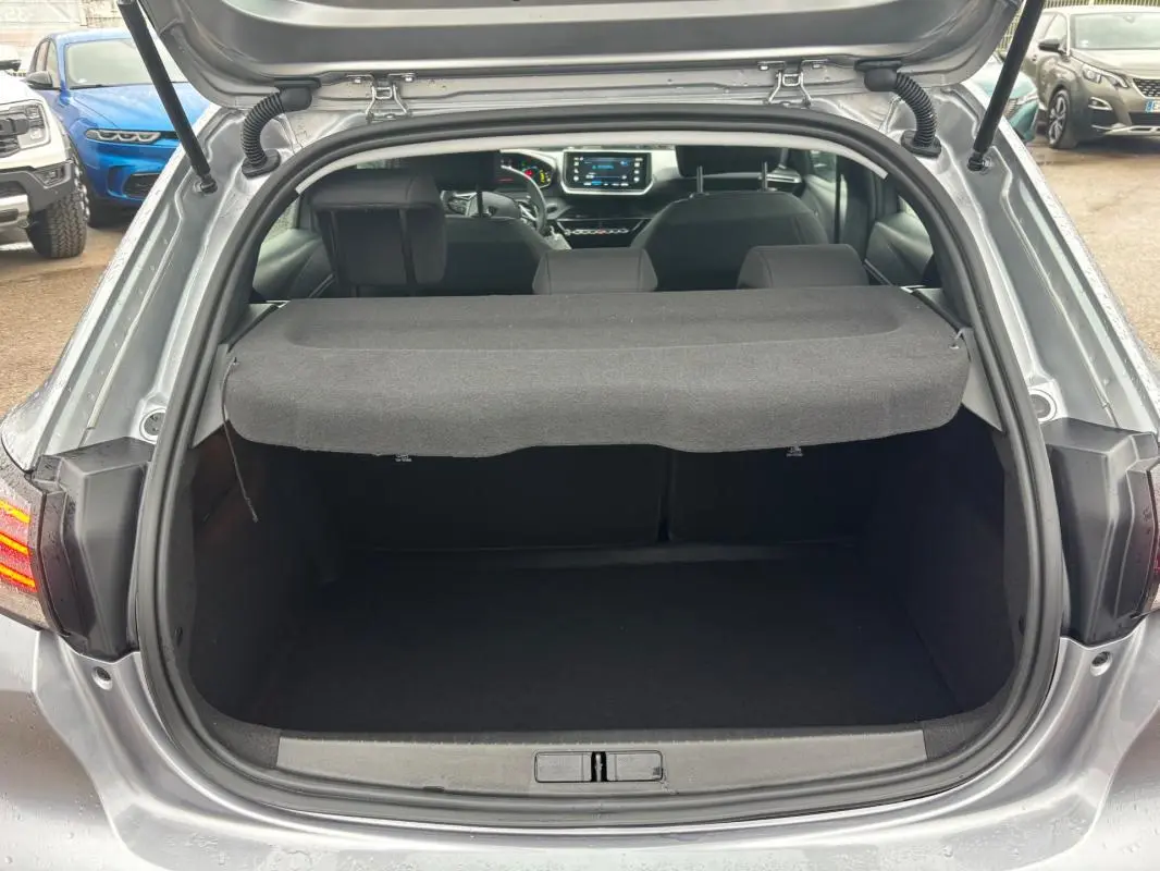 Coffre ouvert d’une Peugeot 208 Hybrid gris 2025, vue arrière montrant l’habitacle et l’écran tactile du tableau de bord.