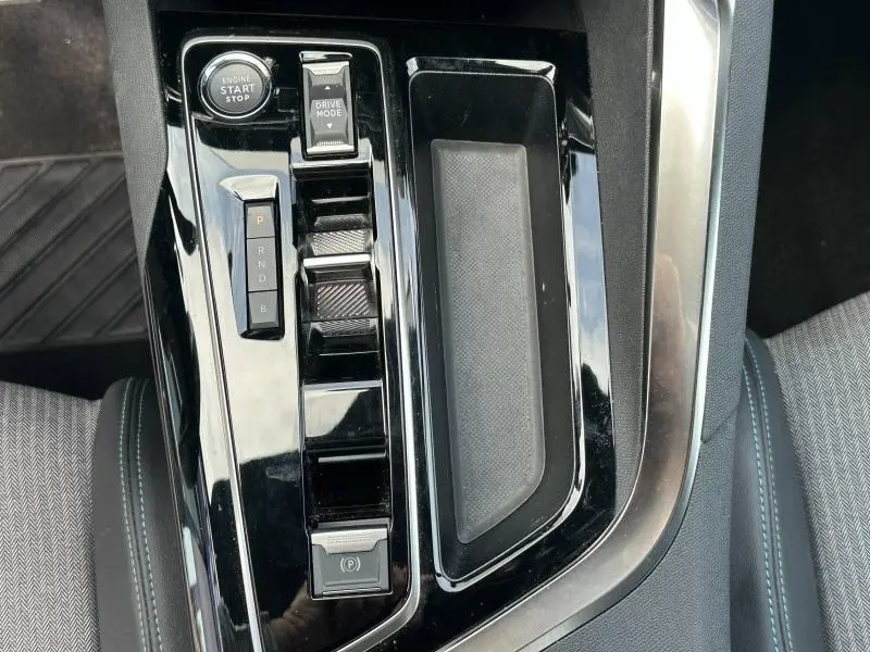 Gros plan sur la console centrale noire brillante du Peugeot 3008 hybride rechargeable 2024 avec bouton start/stop et commandes de boîte auto.