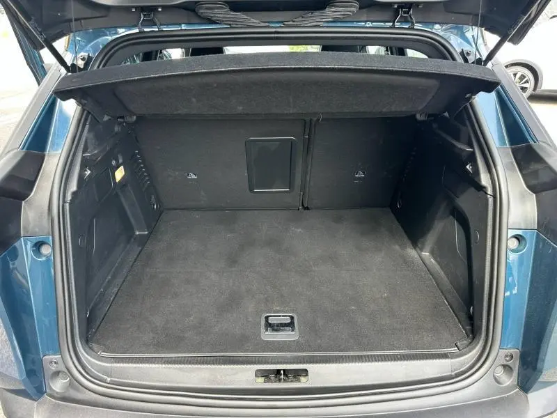 Vue arrière du coffre ouvert du Peugeot 3008 hybride rechargeable bleu, montrant un espace de rangement propre et spacieux.