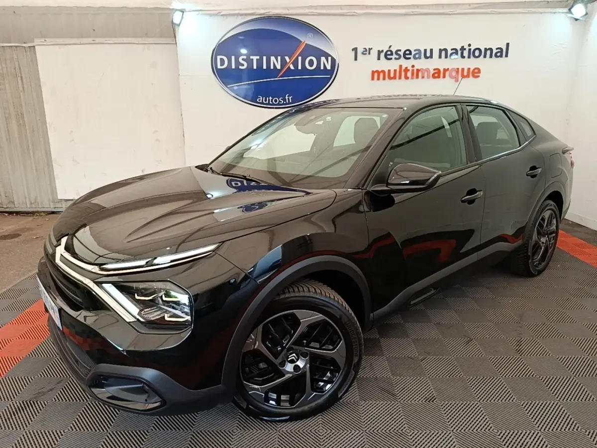 Citroën C4 X noir vue 3/4 avant droit, avec jantes noires et phares LED ellipsoïdaux visibles en intérieur showroom.