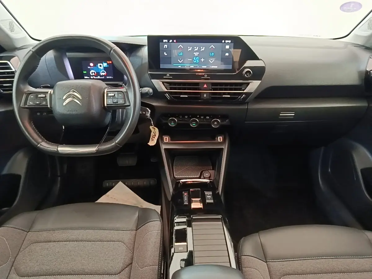 Vue intérieure avant de la Citroën C4 X 2023, tableau de bord noir avec écran tactile central et volant cuir multifonctions.