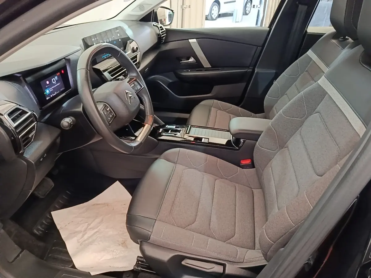Vue intérieure côté conducteur de la Citroën C4 X noire 2023 avec volant cuir multifonctions et sièges tissu gris.
