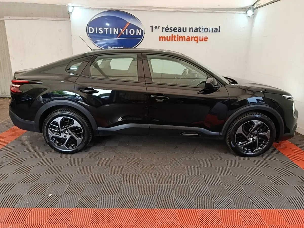 Vue de profil côté gauche d'une Citroën C4 X noire 2023 avec jantes noires et toit légèrement incliné.