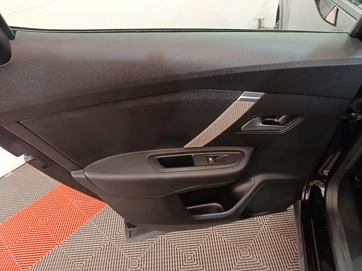Porte intérieure côté gauche de la Citroën C4 X noire, avec poignée, commande de vitre et insert décoratif gris.