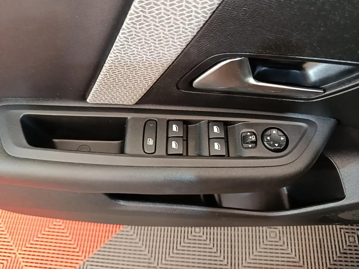 Gros plan sur la commande des vitres et rétroviseurs côté conducteur dans une porte intérieure noire avec insert décoratif gris.