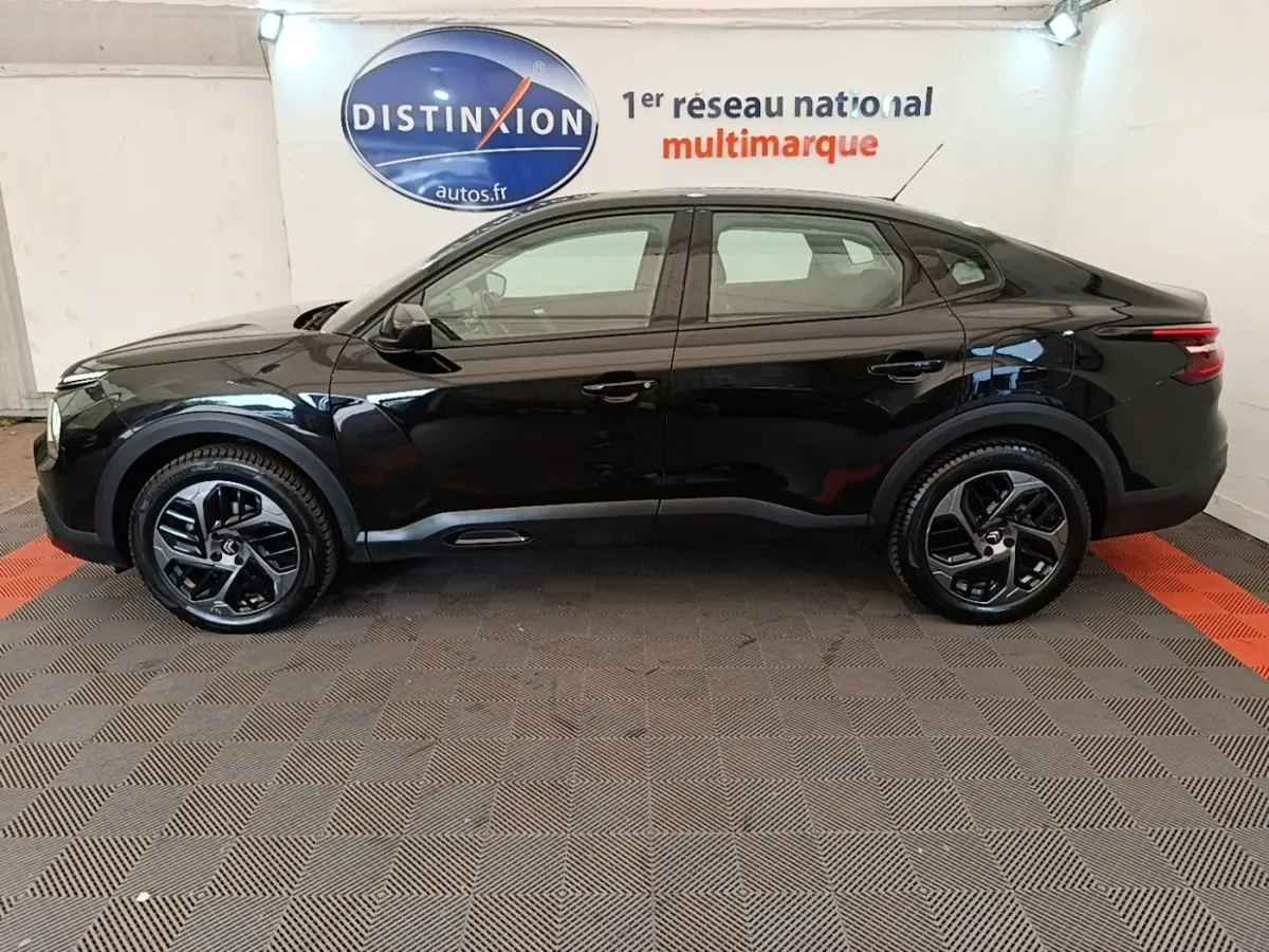 Profil côté gauche de la Citroën C4 X noire 2023 avec jantes noires et lignes fluides, en intérieur showroom.