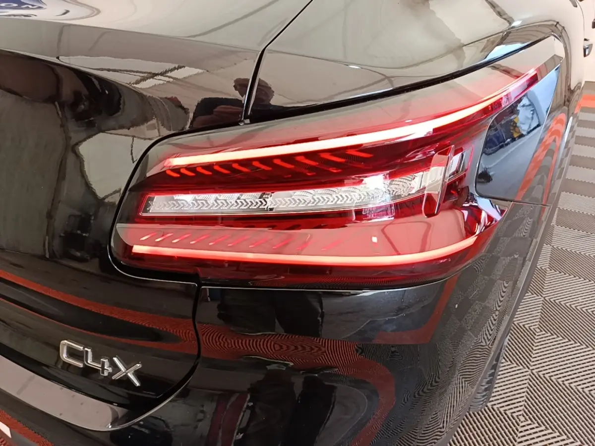 Gros plan sur le feu arrière droit rouge et blanc d'une Citroën C4 X noire avec logo C4 X visible sur la malle arrière.
