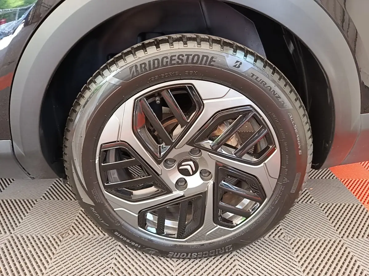 Gros plan sur la roue avant droite noire d'une Citroën C4 X 2023 avec jante alliage au design géométrique.