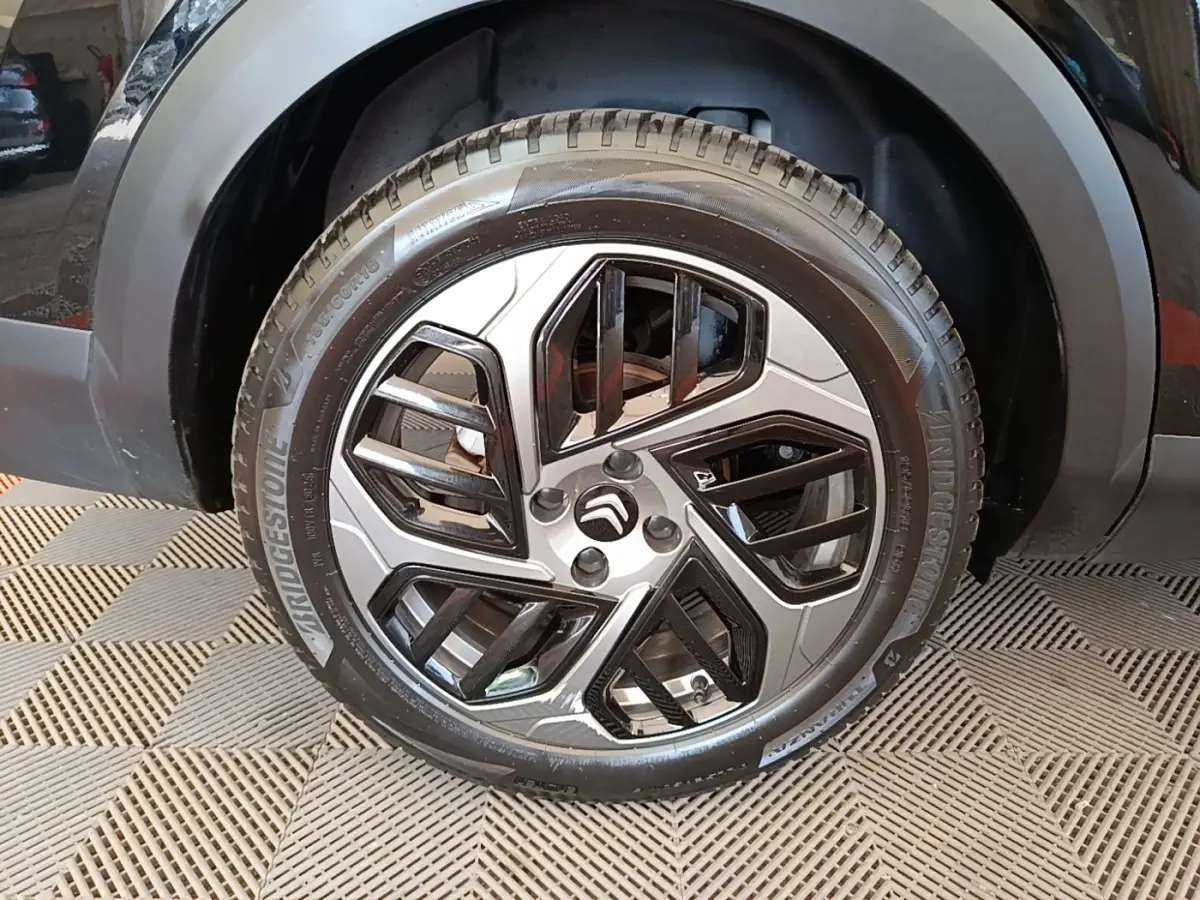 Gros plan sur la roue avant droite noire d'une Citroën C4 X 2023 avec jante alliage au design géométrique.