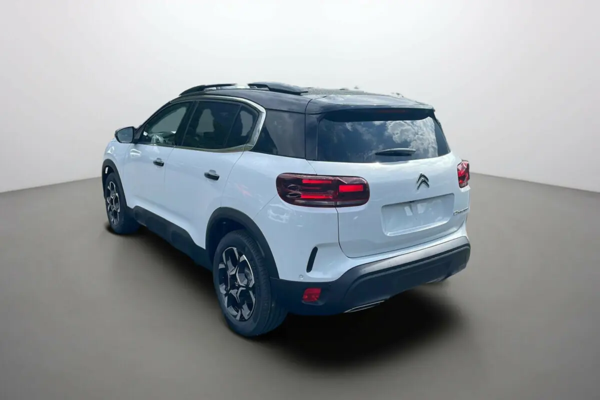 Vue 3/4 arrière droite d'un Citroën C5 Aircross hybride 2025 blanc okénite avec toit noir et jantes distinctives.