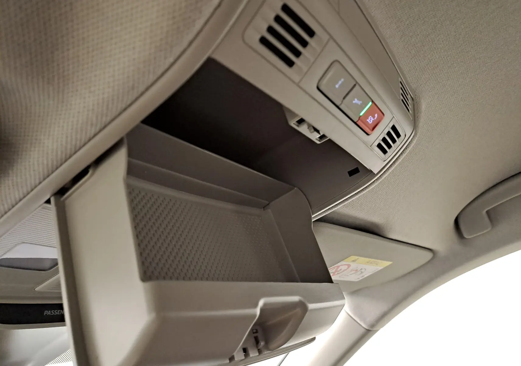 Vue intérieure en plongée du rangement lunettes ouvert sur le plafond du Skoda Kamiq blanc Lune, avec commandes d'éclairage intégrées.