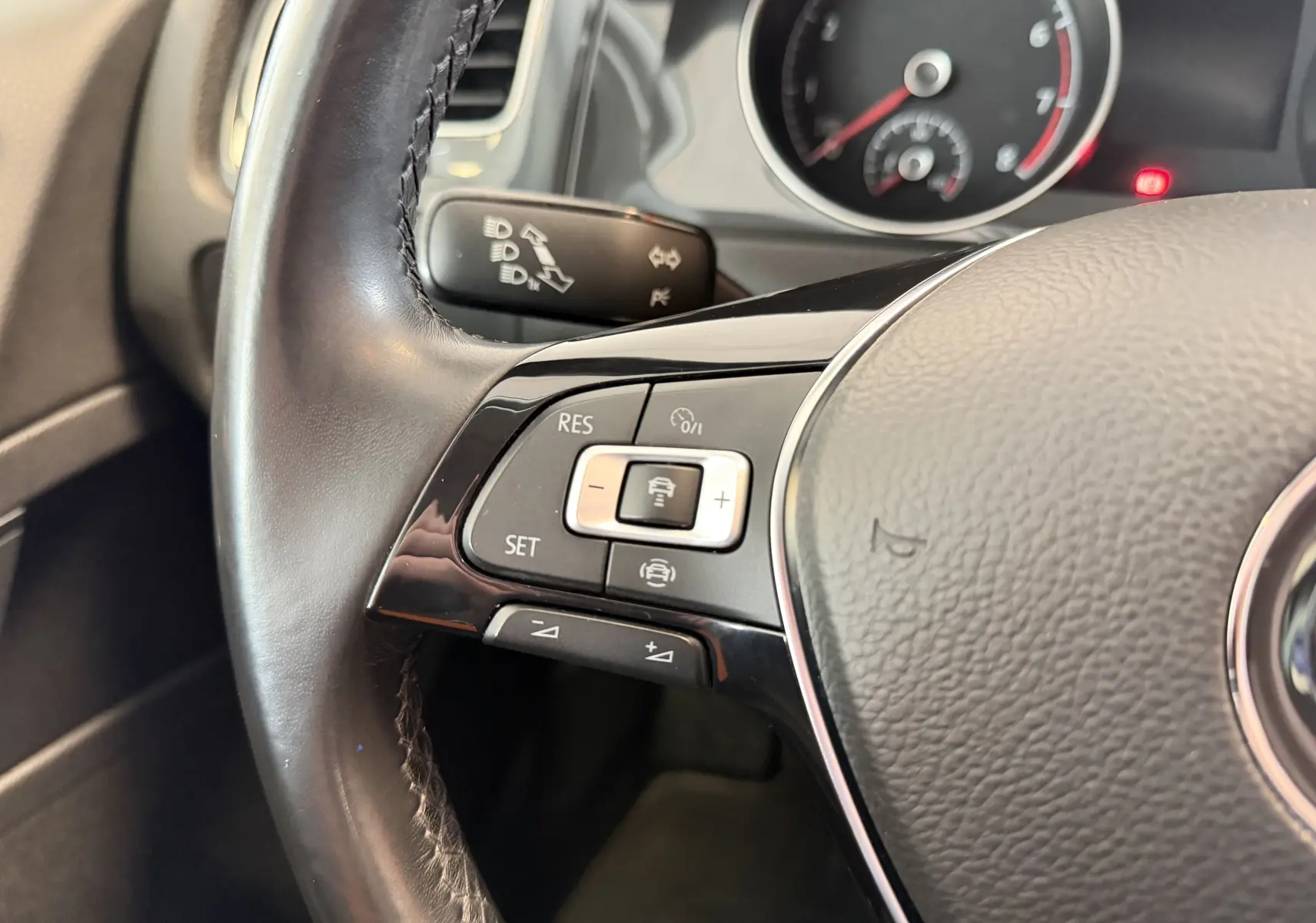 Gros plan sur le volant côté gauche d’une Volkswagen Golf gris, montrant les commandes de régulateur de vitesse et le tableau de bord partiel.