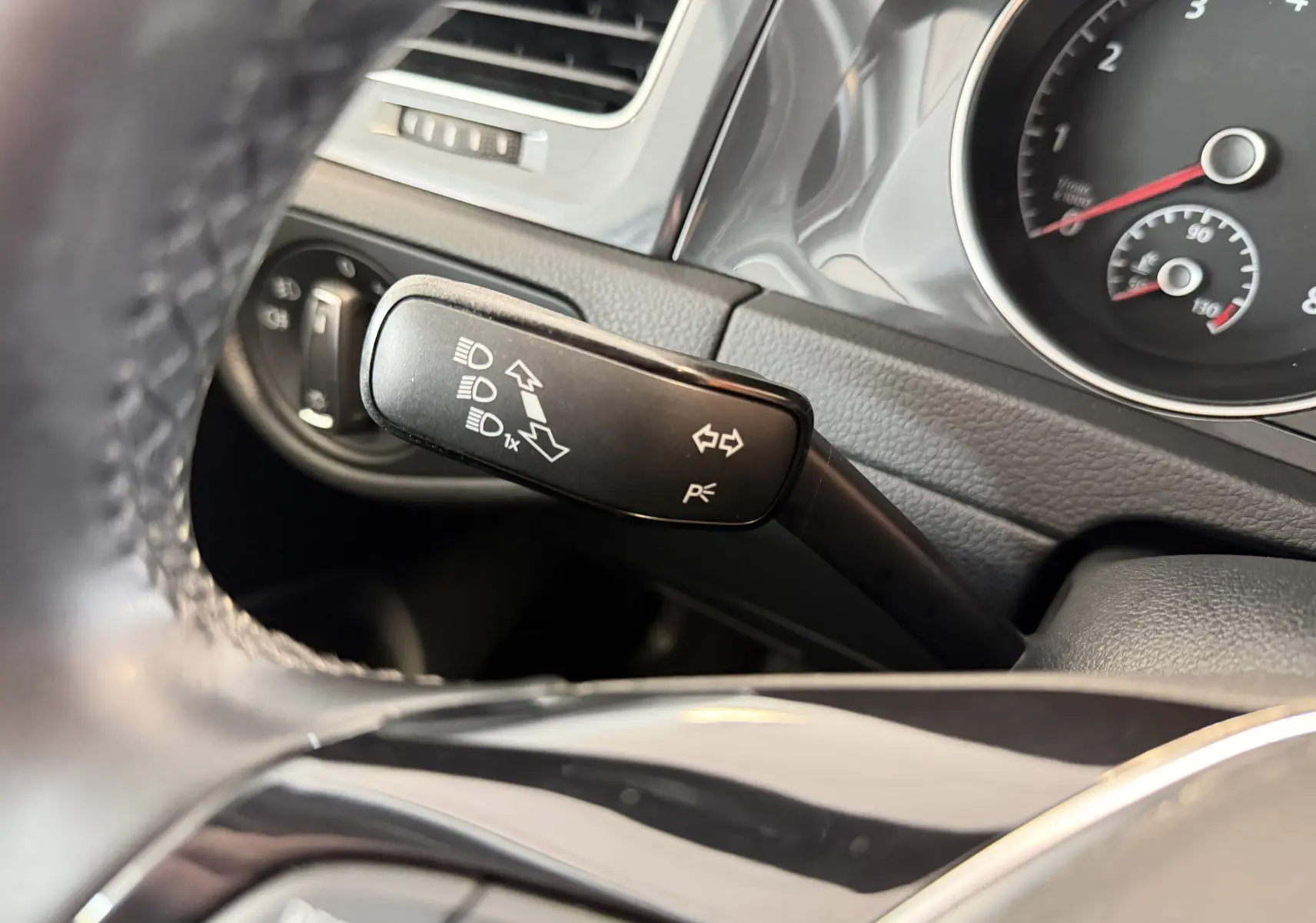 Gros plan sur la manette de clignotant noire du tableau de bord d’une Volkswagen Golf gris, avec compteur partiel en arrière-plan.
