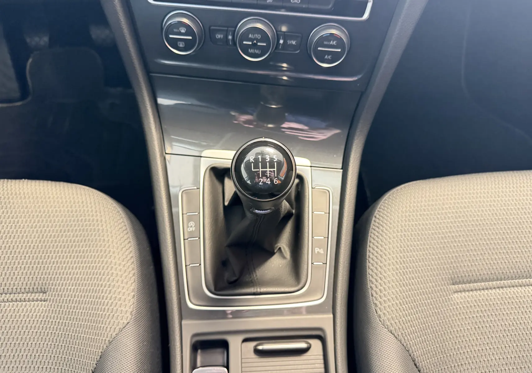 Vue intérieure centrée sur le levier de vitesses manuel de la Volkswagen Golf TSI 130 Confortline gris, entouré des sièges avant.