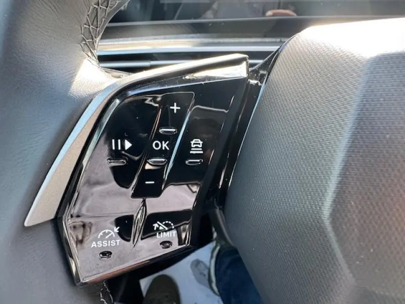 Gros plan sur les commandes au volant noir brillant du Peugeot 5008 Hybrid 2025, avec boutons multifonctions et régulateur de vitesse.