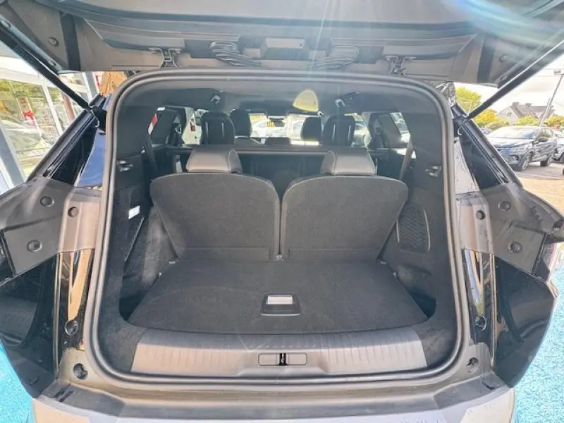 Coffre ouvert vu de l'arrière d'un Peugeot 5008 Hybrid noir Perla Nera, montrant les sièges arrière relevés.