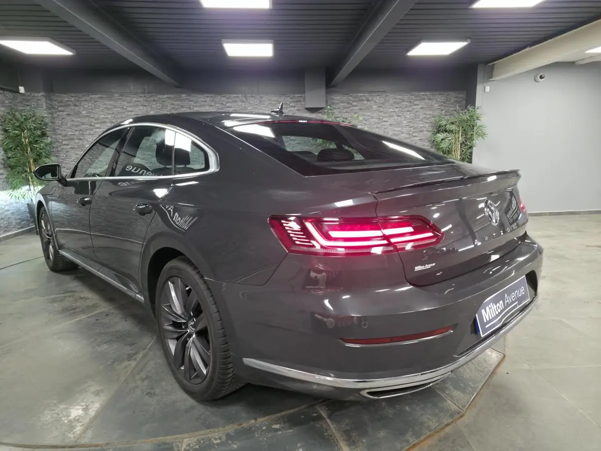 Volkswagen Arteon gris 3/4 arrière droit en intérieur, feux arrière LED allumés et jantes alliage 18 pouces.