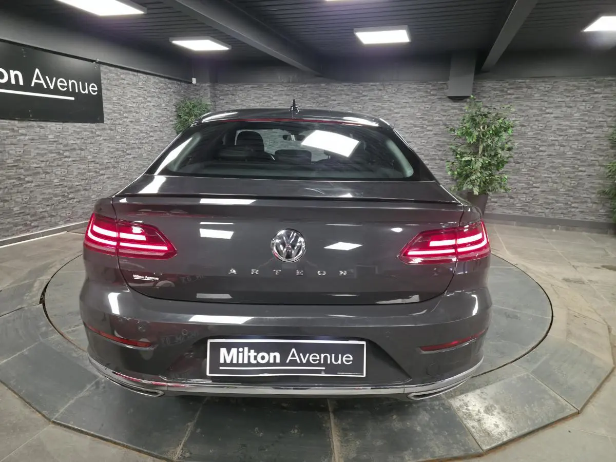 Vue arrière d’une Volkswagen Arteon gris Urano avec feux LED allumés et badge R-Line visible en intérieur showroom.