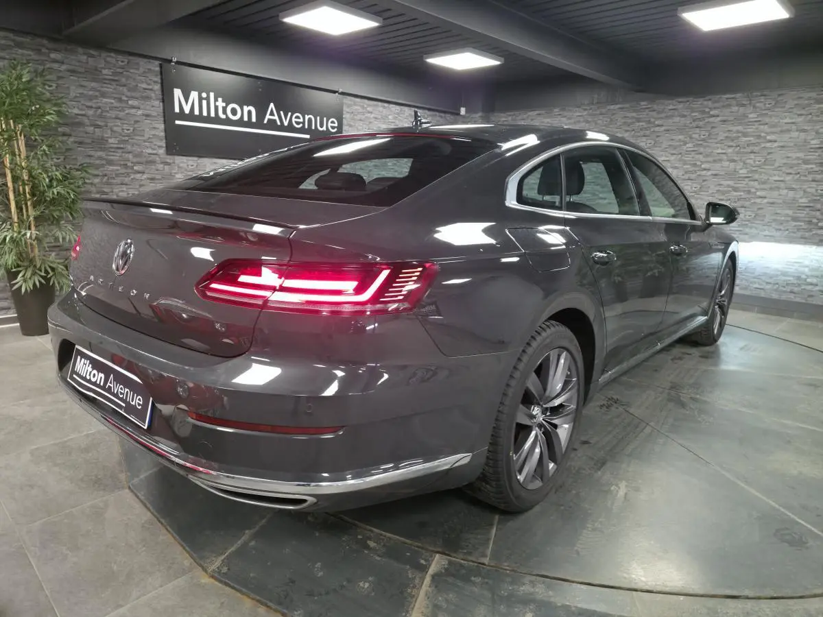 Volkswagen Arteon gris 3/4 arrière droit avec feux LED allumés et jantes alliage 18 pouces en showroom.