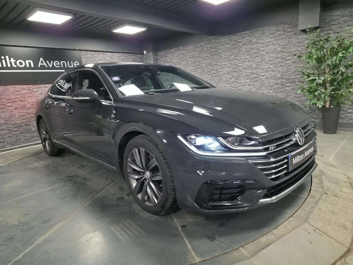Volkswagen Arteon gris 3/4 avant droit en intérieur, avec phares LED allumés et badge R-Line visible.