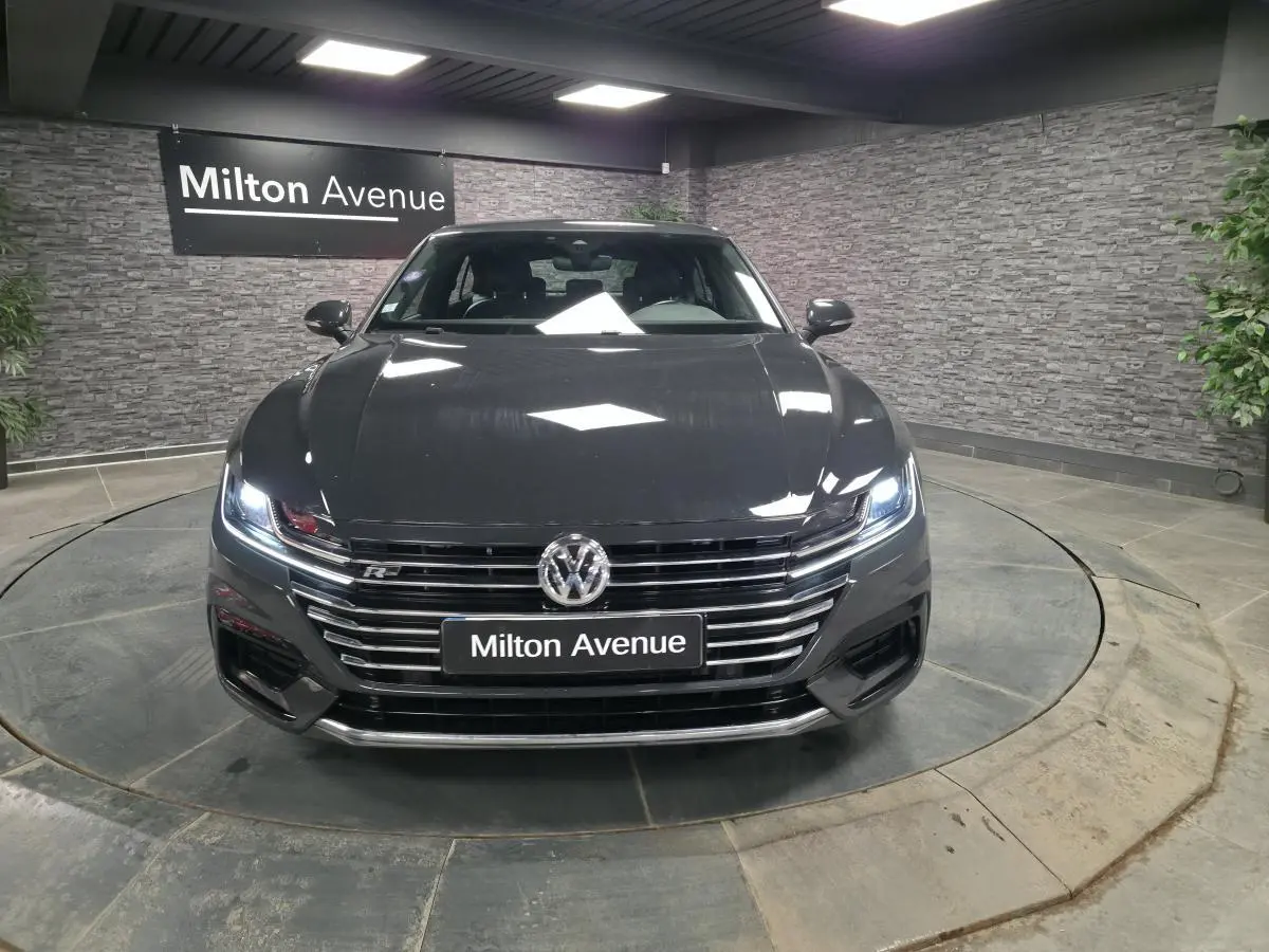 Vue avant d'une Volkswagen Arteon gris Urano avec calandre chromée et phares LED allumés dans un showroom.