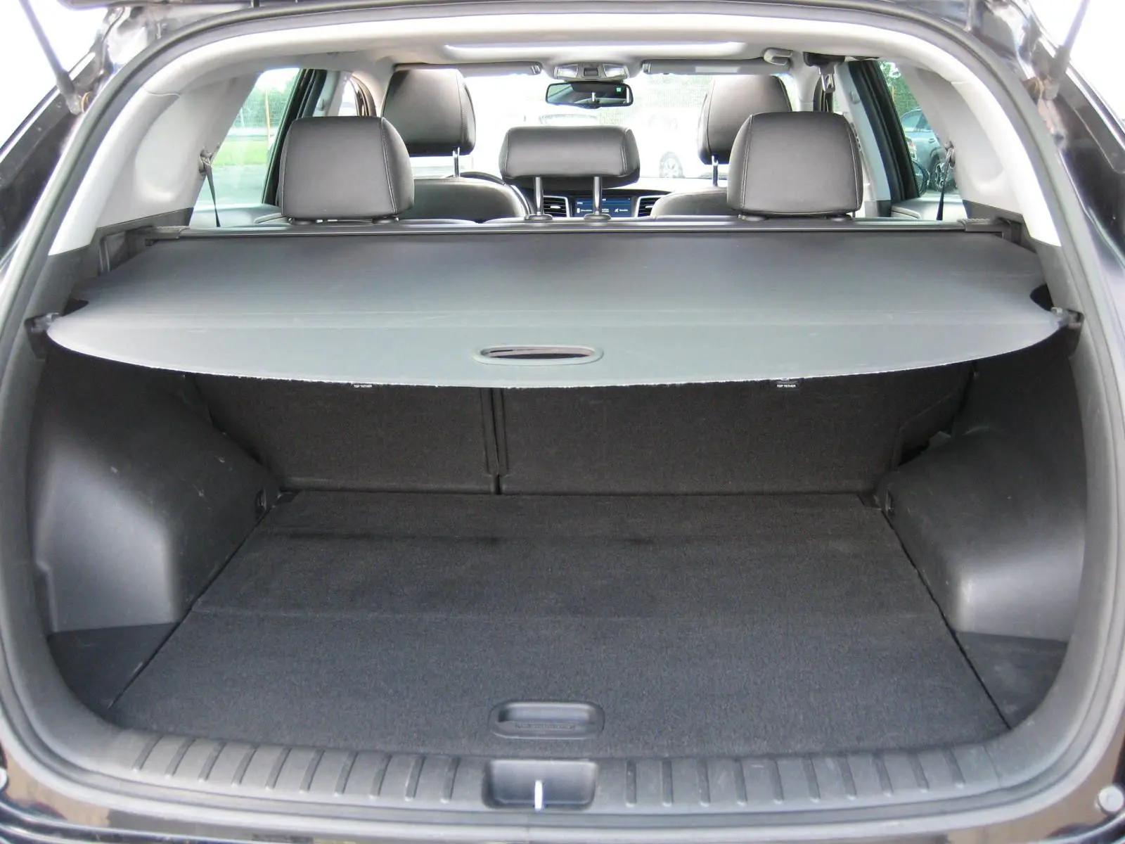 Vue arrière du coffre ouvert du Hyundai Tucson noir Fantom Metal, avec cache-bagages et sièges arrière en cuir visibles.