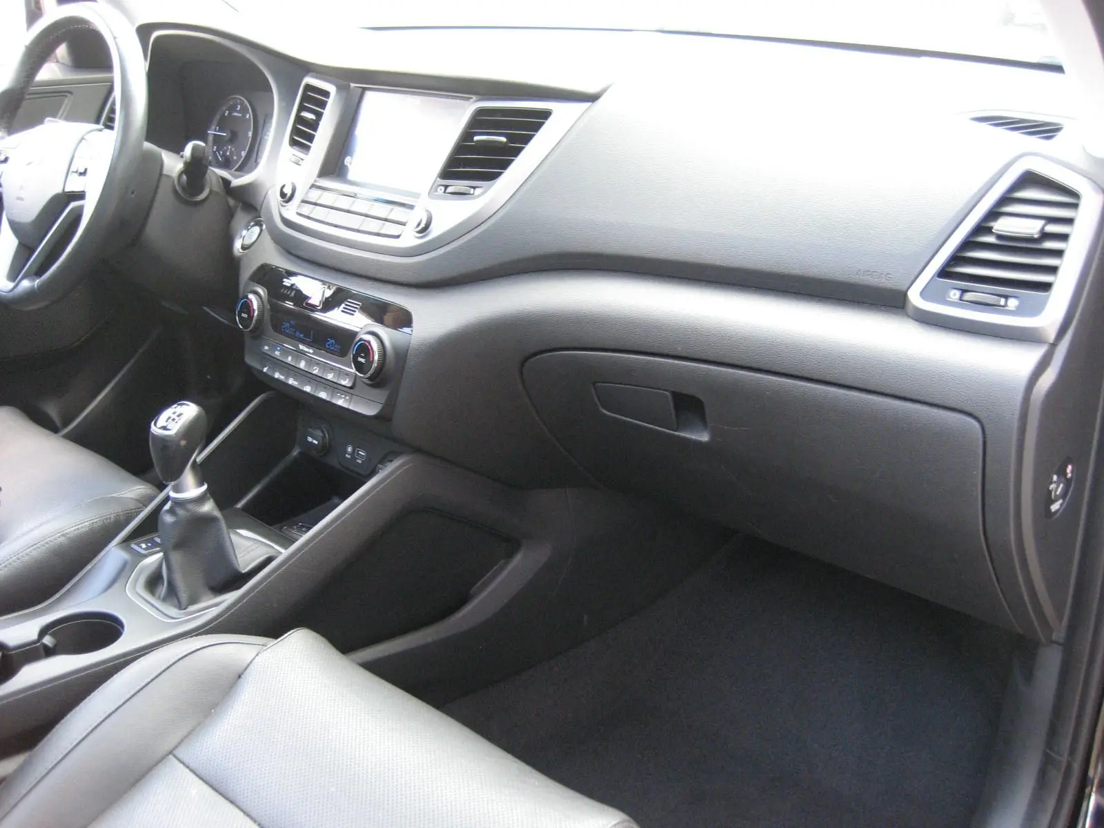 Vue intérieure côté passager du tableau de bord noir du Hyundai Tucson 2016 avec levier de vitesses manuel et sièges cuir.