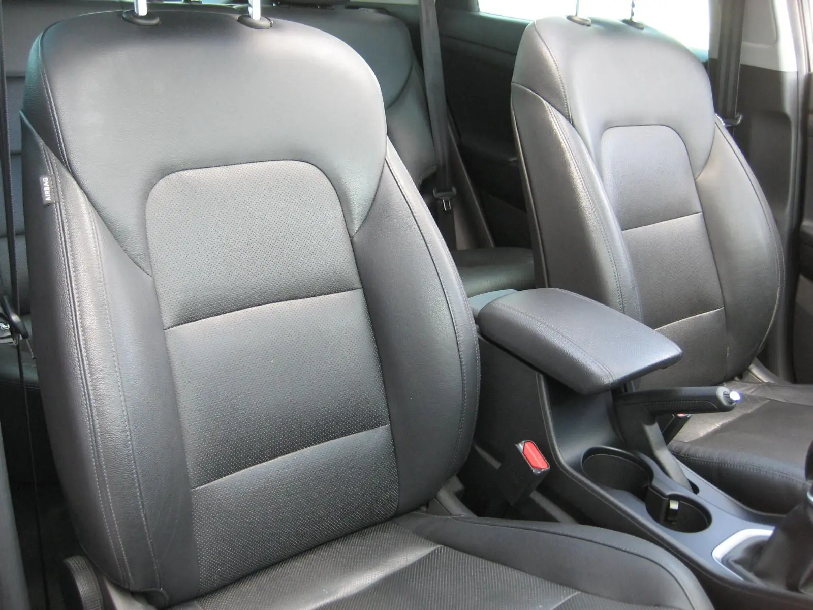 Gros plan sur les sièges avant en cuir noir du Hyundai Tucson 2016, avec accoudoir central et console entre les deux.