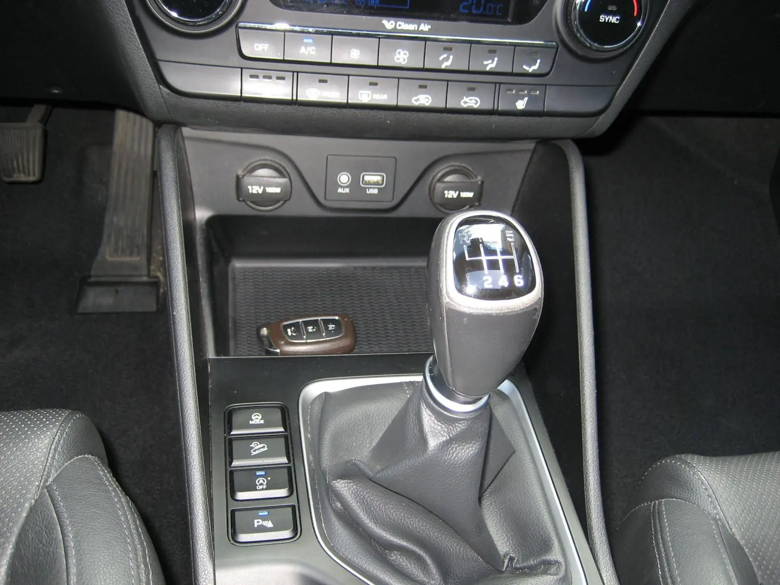 Vue rapprochée de la console centrale noire du Hyundai Tucson 2016, mettant en valeur le levier de vitesse manuel et les commandes adjacentes.