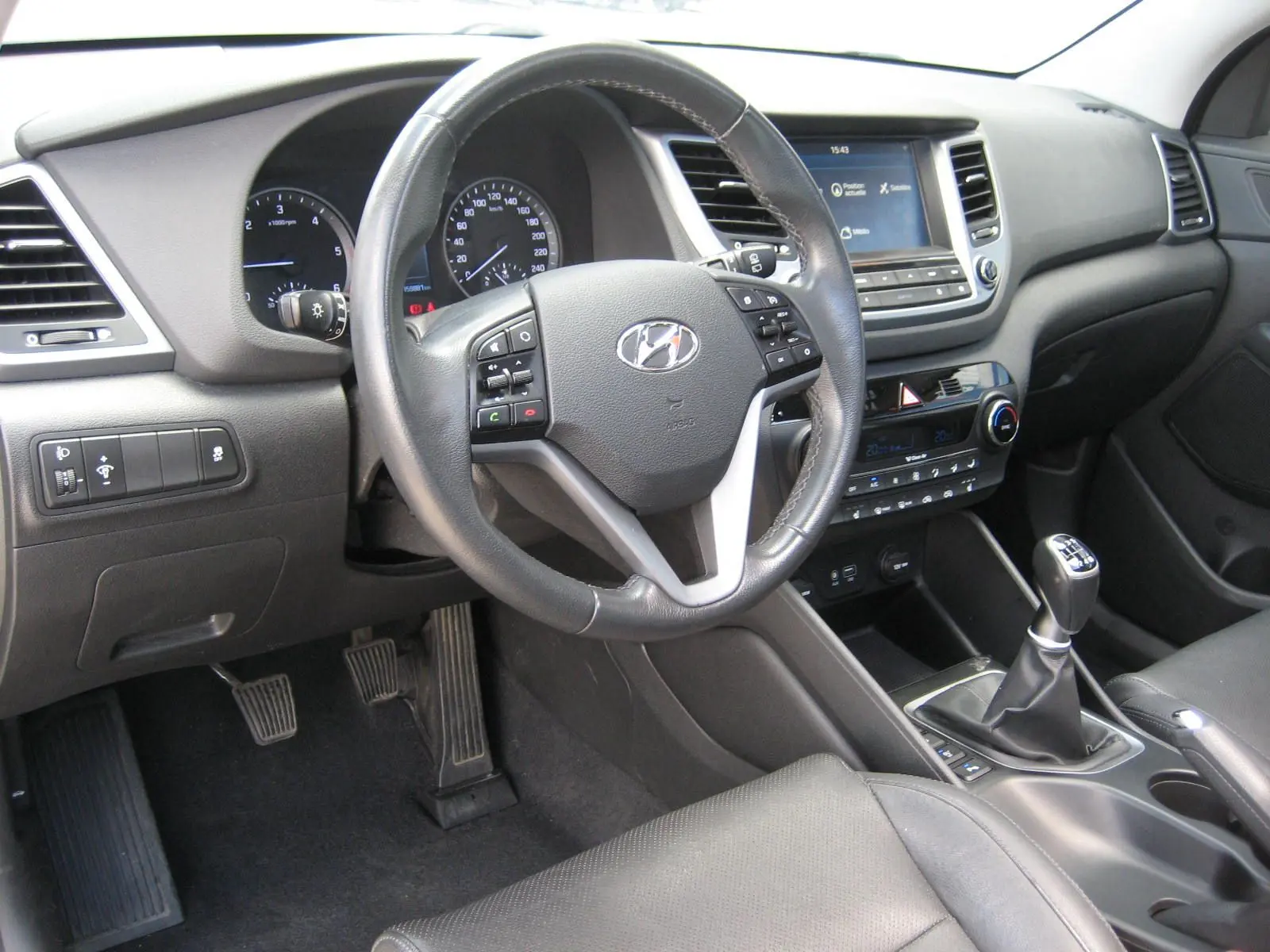 Intérieur du Hyundai Tucson 2016 vu côté conducteur, volant cuir multifonction et tableau de bord avec écran tactile.