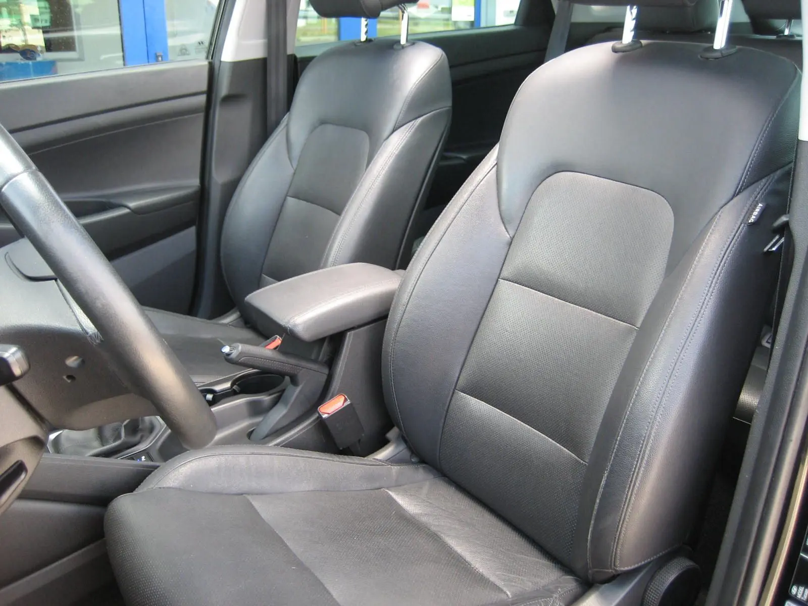 Vue intérieure côté avant droit du Hyundai Tucson 2016, sièges en cuir noir et accoudoir central visible.
