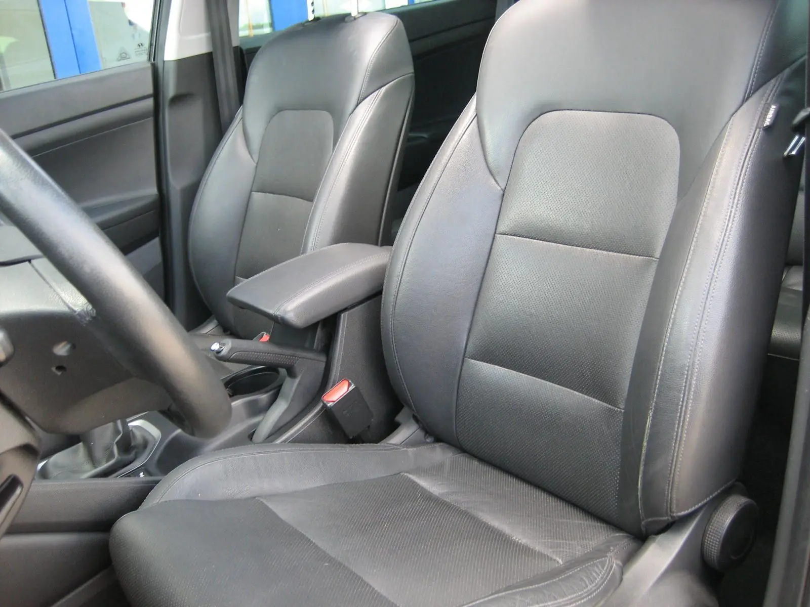 Vue intérieure rapprochée des sièges avant en cuir noir du Hyundai Tucson 2016, avec accoudoir central et volant partiel visible.