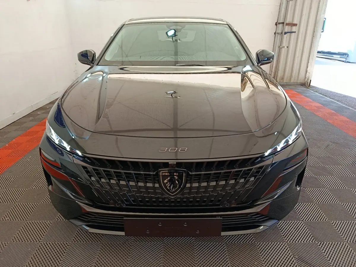 Vue frontale d'une Peugeot 308 noire 2026 avec calandre noire et logo lion central bien visible.