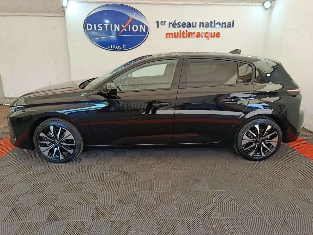 Profil côté gauche de la Peugeot 308 noire 2026 avec jantes alliage bicolores et vitres teintées, en intérieur showroom.