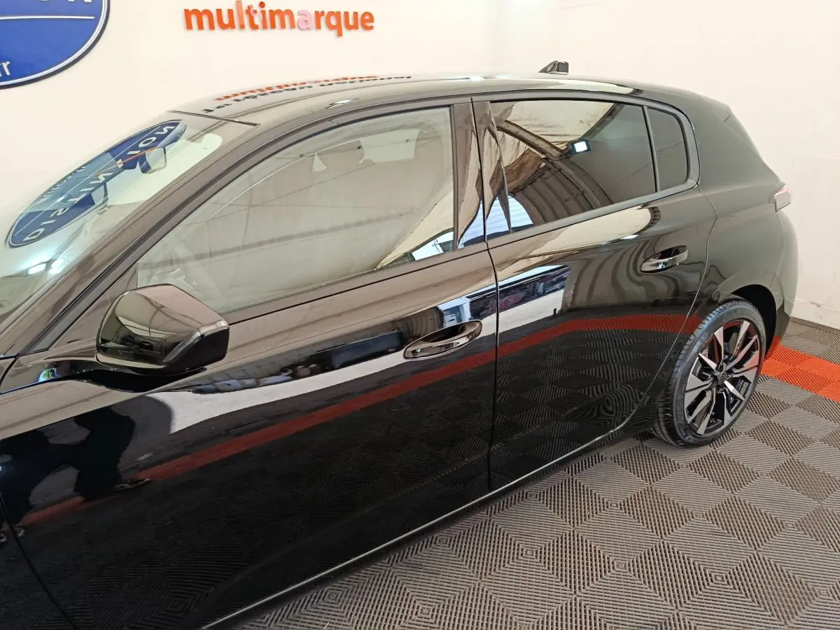 Vue latérale droite d'une Peugeot 308 noire 2026 avec jantes alliage et vitres teintées, sur sol damier intérieur.