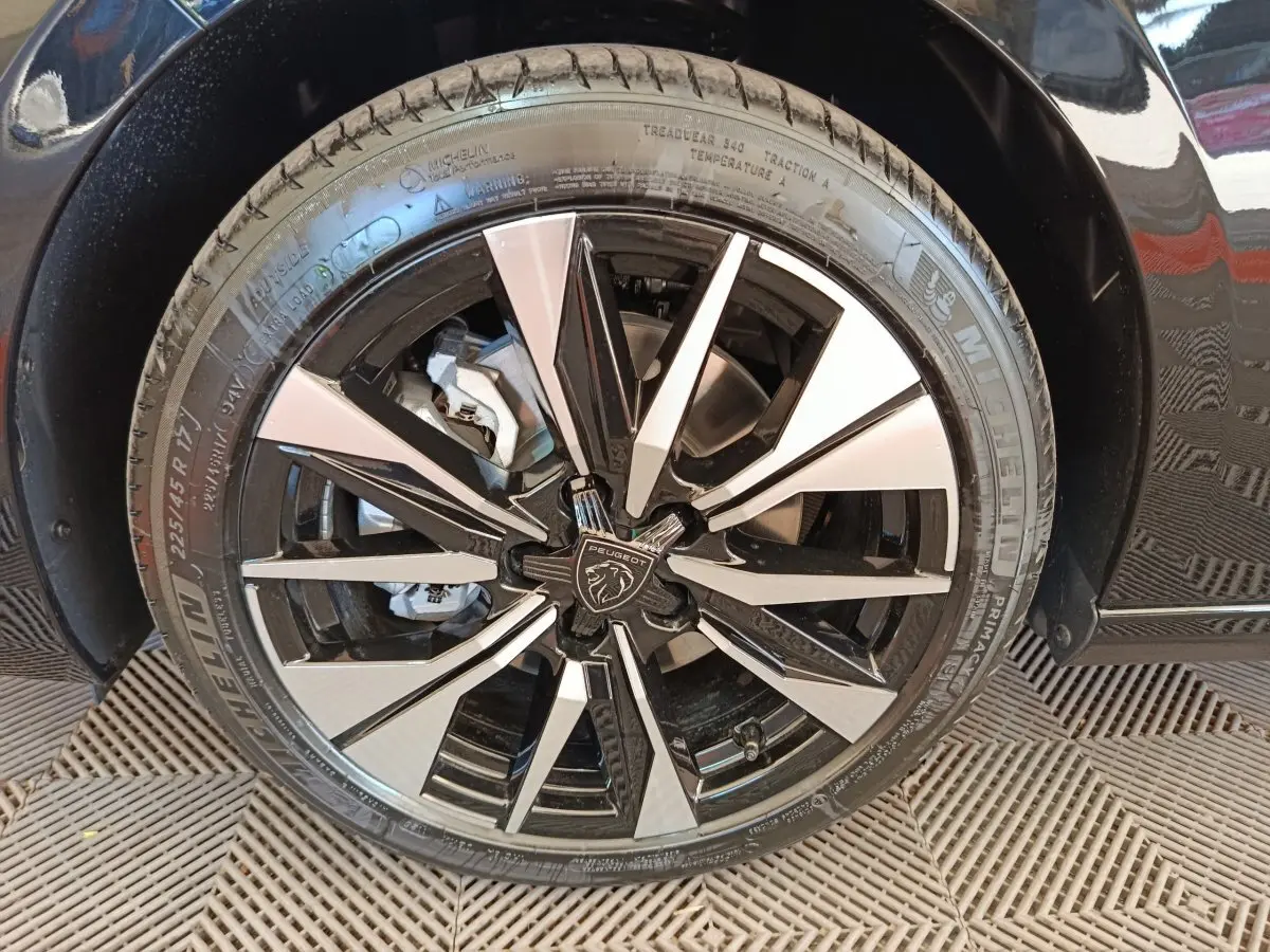 Gros plan sur la roue avant droite noire avec jante alliage bicolore et logo Peugeot au centre.