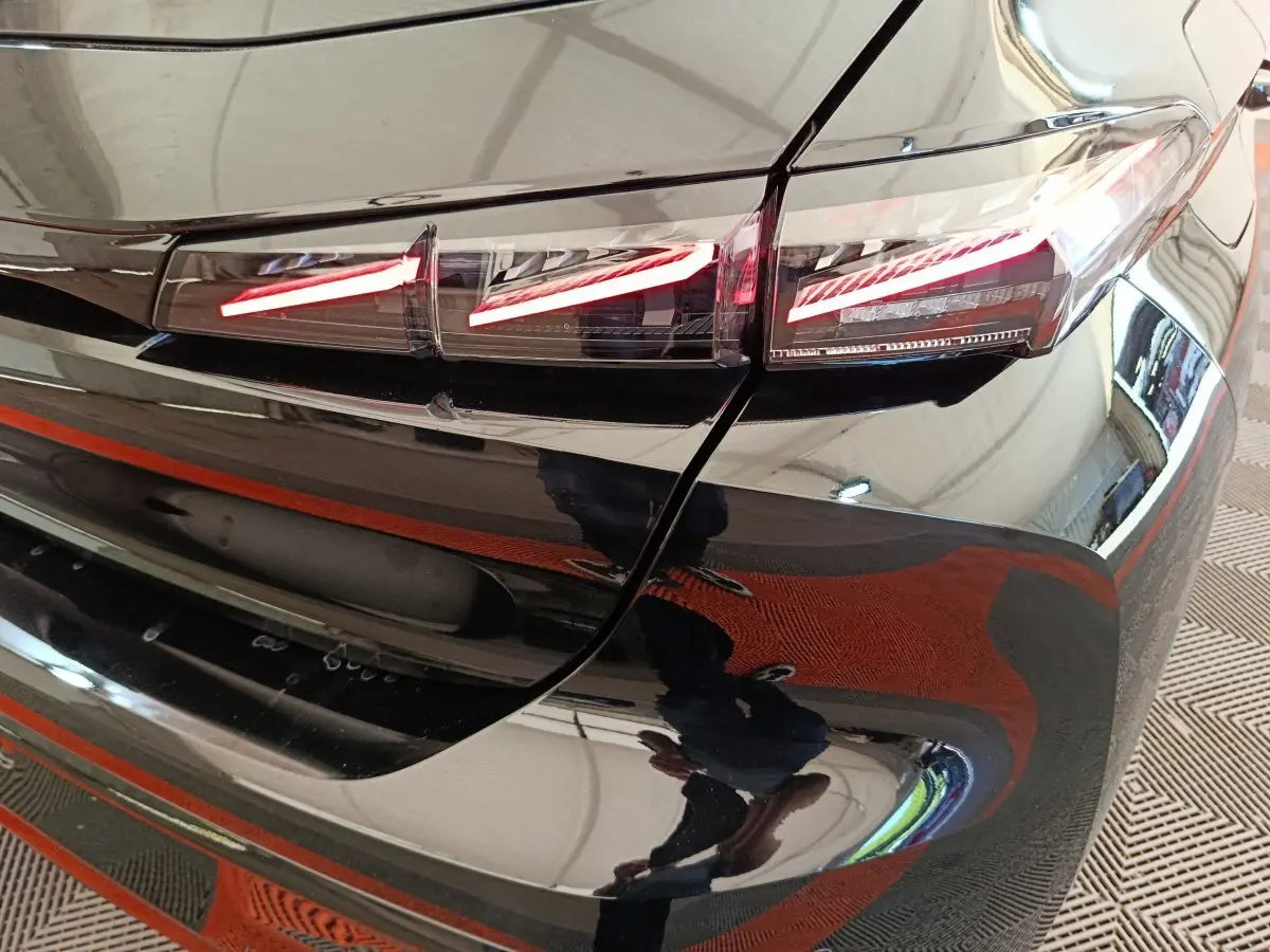 Gros plan sur le feu arrière droit rouge allumé d'une Peugeot 308 noire, reflet brillant sur la carrosserie.