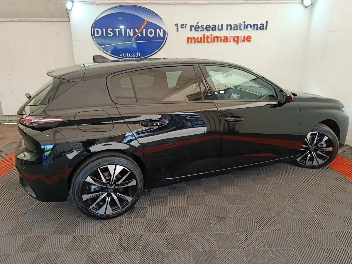 Profil droit d'une Peugeot 308 noire 2026 avec jantes alliage et vitres teintées en intérieur showroom.
