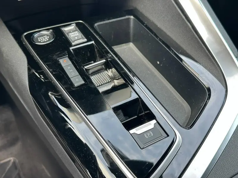 Gros plan sur la console centrale noire brillante du Peugeot 3008 Hybride Rechargeable 2024 avec sélecteur de boîte auto et bouton start/stop.
