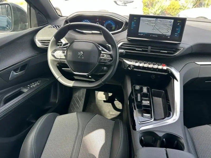 Vue intérieure avant du Peugeot 3008 Hybride Rechargeable 2024, montrant le volant cuir, l'écran tactile et la console centrale noire.